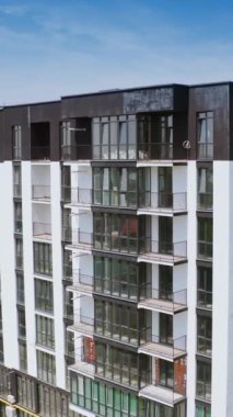 Beyaz ve siyah renkli çok katlı bir bina. Bir sürü penceresi ve balkonları olan yeni inşa edilmiş uzun bir apartmanın dış cephesi. Kamera aşağı iniyor. Dikey video