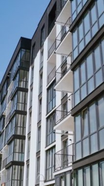 Çok katlı binanın modern cephesi. Mavi gökyüzüne karşı siyah beyaz renkte yeni bir apartman. İHA görüntüsü. Dikey video