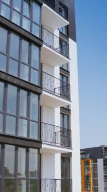 Modern çok katlı bina. Yeni yüksek katlı binanın geniş camlı balkonları. Şehirde modern tasarımı olan siyah beyaz bir apartman. Kamera yükseliyor. Dikey video