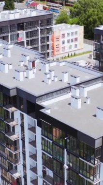 Şehirdeki modern apartmanlar. Modern tasarımın yüksek binaları olan yeni bir yerleşim yeri. Kentsel arka planda çok katlı binaların çatıları. Hava görüntüsü. Dikey video