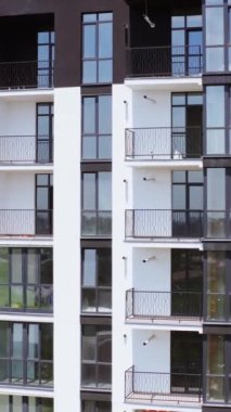 Siyah ve beyaz apartman blokları. Şehirde camlı balkonları olan modern çok katlı bir binanın ön manzarası. Güzel yeni apartmanlar. Dikey video