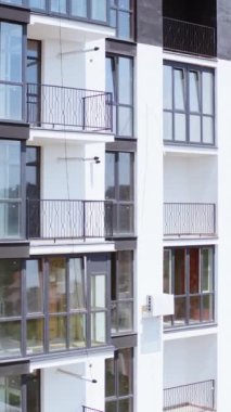 Güzel yeni apartmanlar. Pencerelerinde şehir manzarası yansıması olan yüksek katlı bir binanın modern cephesi. Beyaz ve siyah renkli çok katlı bir bina. Ön manzara. Dikey video