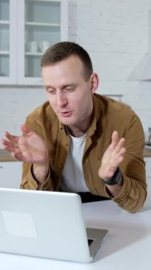 Genç iş adamı evde video görüşmesi yapıyor. Öğrenci mutfak arka planında kablosuz bir dizüstü bilgisayarın önünde konuşuyor. Uzaktan kumanda. Dikey video