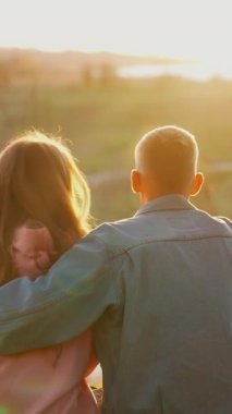 Romantik çift doğada dinleniyor. Genç insanlar birlikte çimenlerde oturup gün batımını seyrediyorlar. Açık havada aşık bir çift. Dikey video