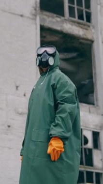 Koruyucu giysili ve gaz maskeli bir adam yıkılmış binanın arka planında duruyor. Kıyametten sonraki dünya kavramını. Dikey video