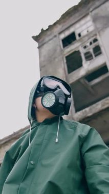 Solunum cihazı ve koruyucu ceketli bir kadın. Penceresiz yıkık binanın arka planında hayatta kalan, şehirdeki kimyasal kirlilik. Aşağıdan bak. Dikey video
