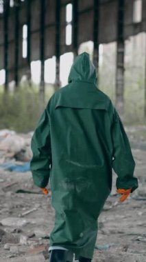 Terk edilmiş çöplerle dolu bir yerde. Koruyucu kıyafetli bir ekolojist yıkılmış binanın içinde yürüyor. Arkadan bak. Yıkılmış bir yer. Dikey video