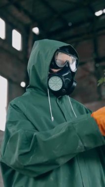 Hastalıklı bölgede çiçekli bir kazazede. Koruyucu kıyafetli ve gaz maskeli bir insan terk edilmiş bir binada çiçek tutuyor. Doğayı kurtar. Ekolojik felaket. Dikey video