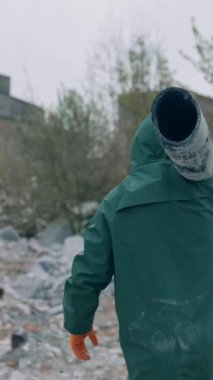 Nükleer kimyasal savaştan sonra hayatta kalan. Kirlenmiş binaların arka planında terk edilmiş bir yerde borular taşıyan güvenli elbiseli bir adam. Dikey video