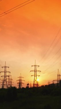 Kırmızı gökyüzü altındaki iletişim hatları. Doğada kabloları olan yüksek voltajlı elektrik kuleleri güzel bir günbatımında. Güç hatları batan güneşin arka planına karşı. Dikey video