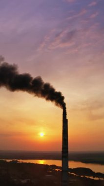 Endüstri yüzünden atmosferdeki kara dumanlar. Güneş batarken baca tüttürmek çevreyi kirletiyor. Akşamları nehir kenarında zararlı bir sanayi tesisi. Dikey video