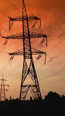 Kırmızı günbatımına karşı yüksek voltajlı elektrik hatlarının desteği. Güneş batışı ve güç hattı pilonu destansı günbatımı gökyüzünde. Dikey video