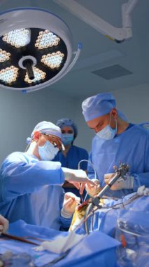 Cerrahi lensler takan baş cerrah hastayı ameliyat ederken oturur. Doktor duman çıkaran elektrikli aletler kullanıyor. Dikey video.