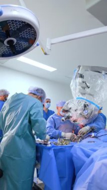 Erkek sıhhiyeci cerrahi standında aletleri düzenliyor. İki cerrah mikroskop kullanarak ameliyat yapıyor. Dikey video.