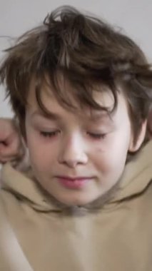 Kafkasyalı genç kazağının kapüşonunu takıyor. Kameraya bakan gülümseyen bir çocuğun portresi. Kapatın. Dikey video