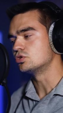 Şarkıcı stüdyoda bir şarkı kaydediyor. Erkek oyuncu profesyonel mikrofonun önünde duruyor ve kulaklık takıyor. Dikey video
