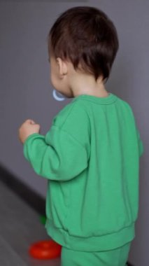 Açık yeşil takım elbiseli küçük bir çocuğun odanın önünden geçişi. Çocuk yerden oyuncakları toplamak için oturur. Dikey video