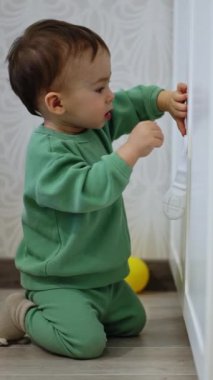 Yeni yürümeye başlayan çocuk dizlerinin üstünde dolabı açmaya çalışıyor. Çocuk düşer, ağlar ve sonra tekrar dener. Dikey video