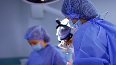 Kadın tıbbi personel beyin cerrahına ameliyatta yardım ediyor. Ameliyathanede çalışan profesyonel sağlık görevlileri. Bulanık arkaplan.