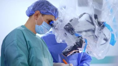 Beyin cerrahı mikroskop dürbünlerine dikkatlice bakar. Ameliyat yapan doktorun yan görüntüsü.