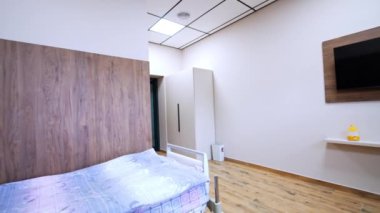 Duvarında televizyon olan rahat, modern hastane koğuşu. İki yatak için geniş bir oda. Odanın etrafında daire çiz ve koridora çık..