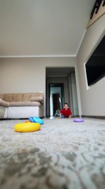 Beyaz, kırmızı tişörtlü ve mavi pantolonlu bir çocuk odaya giriyor. Mutlu çocuk kameraya sevimli bir gülümsemeyle yaklaşıyor. Düşük açı. Dikey video.