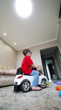 Küçük bebek evde oturup oyuncak araba kullanıyor. Küçük çocuk evde oyun oynuyor. Düşük açı. Dikey video.
