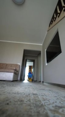 Enerjik bebek çocuk odaya koşup oyuncak arabası itiyor. Evde oynayan çocuğa düşük açılı bakış açısı. Dikey video.