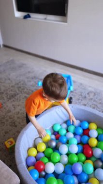 Tatlı çocuk kuru havuza düşer. Küçük çocuk renkli topların arasında yatıyor. Üst Manzara. Dikey video.