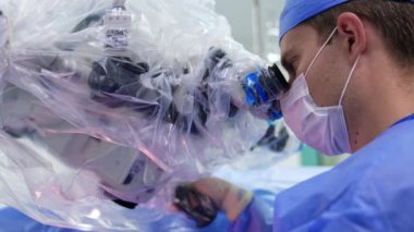Modern mikroskobun dürbününe odaklanmış beyaz bir erkek cerrah görünüşü. Profesyonel bir doktorun ameliyat yaparken çekilmiş bir portresi. Kapat..