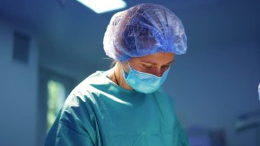 Beyaz kadın cerrah metal makas ve iplik kullanıyor. Ameliyat hemşiresi doktora ameliyatta yardım ediyor..
