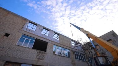 Crane inşaat halindeki binada duruyor. Yeni pencereler ve beyaz tuğlalardan oluşan evde bir duvar parçası. Düşük açı görünümü.