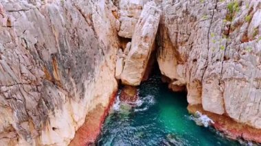 Denizin şaşırtıcı maviliği çıplak kayalıklardaki mağaraya yaklaşıyor. Yeşil otlar dağın tepesindeki vadiyi kaplıyor..