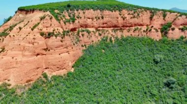Yeşil çimenler ve yosunlarla kaplı dağın yamacına doğru uçuyorlar. Yeşilliklerin arasında kayanın tepesinde iki kişi duruyor..