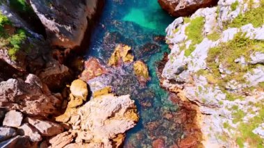 Kayalıklar arasındaki berrak turkuaz suyun nefes kesici görüntüsü. Resimli kayaların arasındaki su manzarasının en üst görüntüsü.