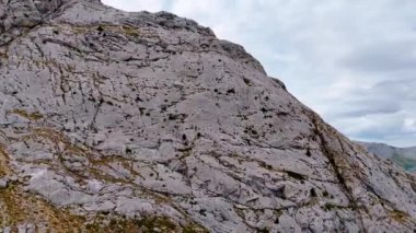 Çıplak gri dağın yamacındaki görüntüler. Bulutlu gökyüzünün altındaki kayanın eteğindeki gölün manzarası.