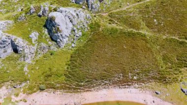 Çim ve yosunlarla kaplı yüksek kayalar. Dağın eteğindeki mavi göl. Güneşli bir günde gökyüzü perspektifi.