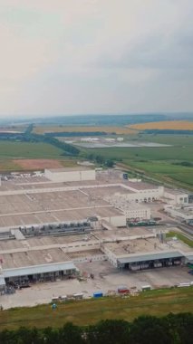 Yeşil alanlarla çevrili modern endüstriyel binanın havadan görünüşü. Büyük modern üretim fabrikası Dikey video
