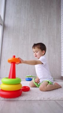 Kafkasyalı çocuk yerde oturup bir piramit inşa ediyor. Evde yerde oyun saatiniz kutlu olsun. Dikey video.