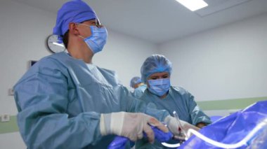 Kendine güvenen bir cerrah cerrahi alet uygular ama doğrudan monitöre bakar. Travma ameliyatında kadın hemşire doktora yardım ediyor. Düşük açı görünümü.