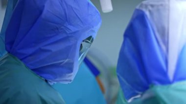 Koruyucu kasklı ve mavi cüppeli bir cerrah operasyonda çalışıyor. Bir doktorun iyileşme travması portresi..