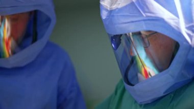 Travma ameliyatında iki erkek cerrah koruyucu kask takıyor. Operasyonda çalışan ortopedinin portresi. Kapat..