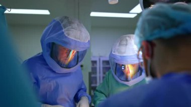 Ortopedik operasyonda çalışan koruyucu kasklı, kendinden emin erkek cerrahlar. Ameliyatta işbirliği yapan odaklanmış doktorlar.