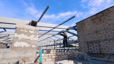 İskelede duran erkek işçi metal direkleri kaynaklıyor. Çatı için çerçeve oluşturuluyor.