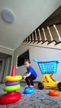 Bebek evde oyuncaklarıyla oynuyor. Küçük çocuk oyuncak piramidinin detaylarıyla dolu arabasını boşaltıyor. Düşük açı. Dikey video.