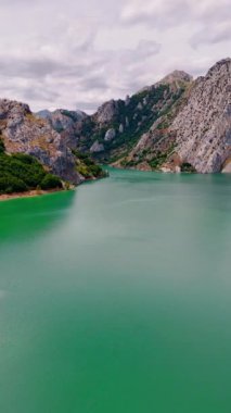 Turkuaz su yüzeyinin göz kamaştırıcı pürüzsüz yüzeyi resim gibi kayalarla çevrili. Yaya olarak göl manzaralı güzel dağlar ve arka planda dramatik bulutlar. Dikey video.