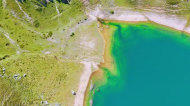 Turkuaz deniz manzaralı, kumlu bir uçuş. Suyun etrafındaki kayalar arasında yosunlar ve zambaklarla kaplı eğimli bir arazi..