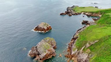 Su manzarasındaki kayaları kaplayan yeşil çimenler. Bazı çıplak kayalar su oluşturur. Hava görünümü.