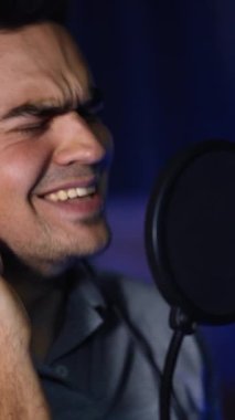Stüdyodaki duygusal şarkı performansı sırasında gözlerini kapatan adam. Karanlık stüdyonun bulanık arka planında yakın plan portresi. Dikey video