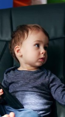 Siyah deri sandalyede oturan küçük, ciddi bir çocuk. Güzel çocuk uzaktan kumandayı elinde tutuyor ve düğmelere basıyor. Dikey video